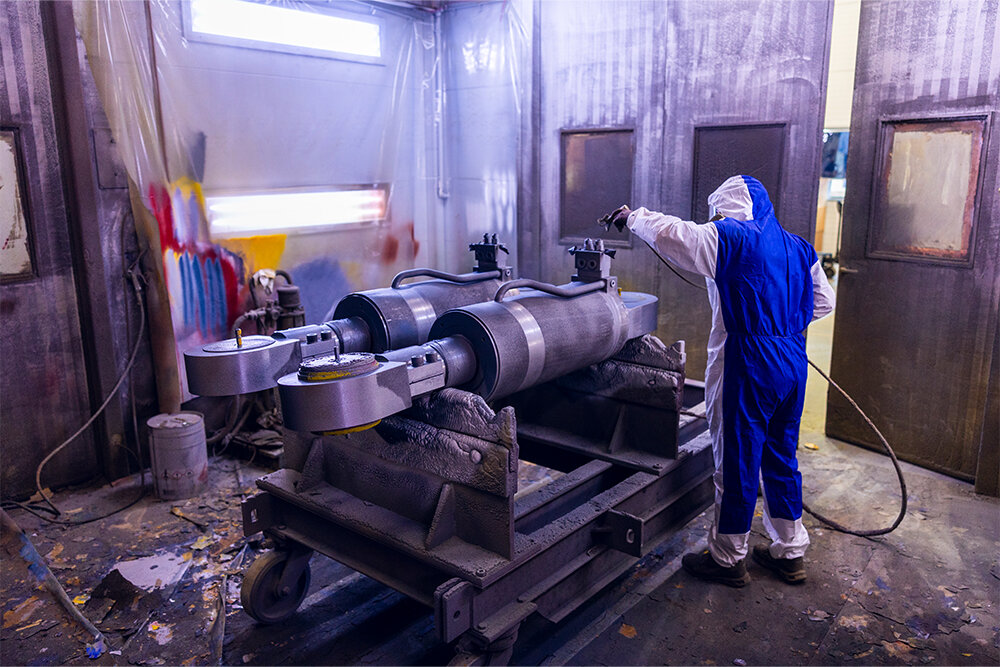 bilde av mann som overflatebehandler to sylindre med malefrakk og verneutstyr