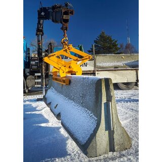An image of a guardrail lifting clamp from BSV lifting a large concrete block seen from the side. There is snow on the ground and around the construction site, and the concrete block is securely suspended in the air.