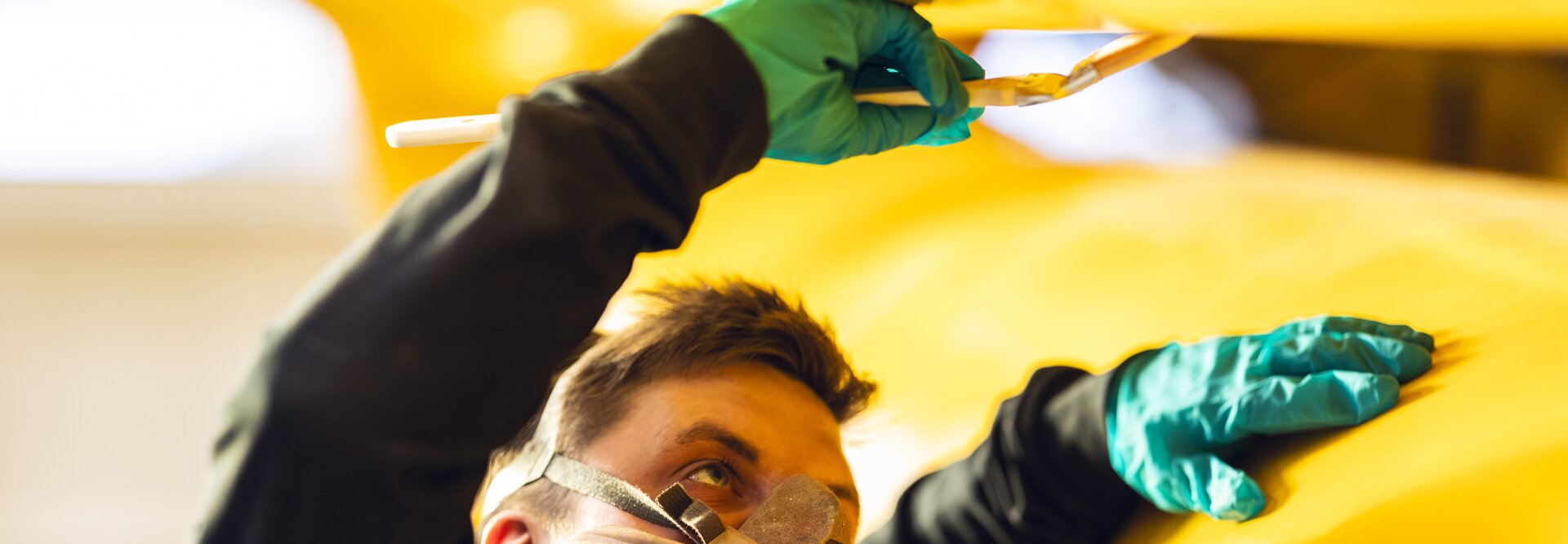 Person har på maske mens han flekker gul maling på en stor hydraulisk demper