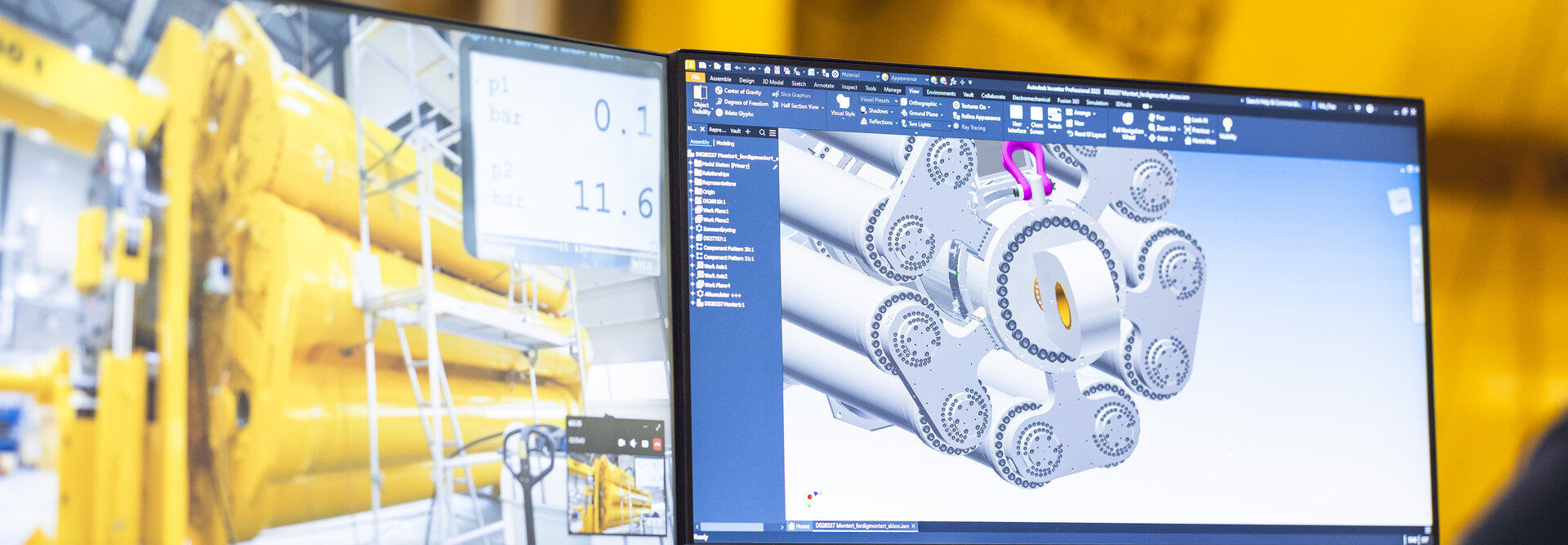 A person sits and looks at a 3D drawing of a hydraulic shock absorber in front of the shock absorber