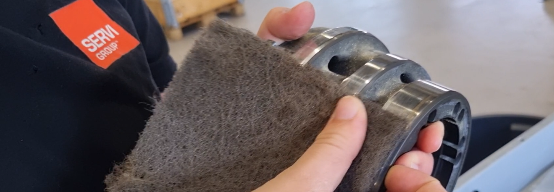 Nærbilde av ripe som pusses bort på poclain motor med Servi Group logo på t-skjorte