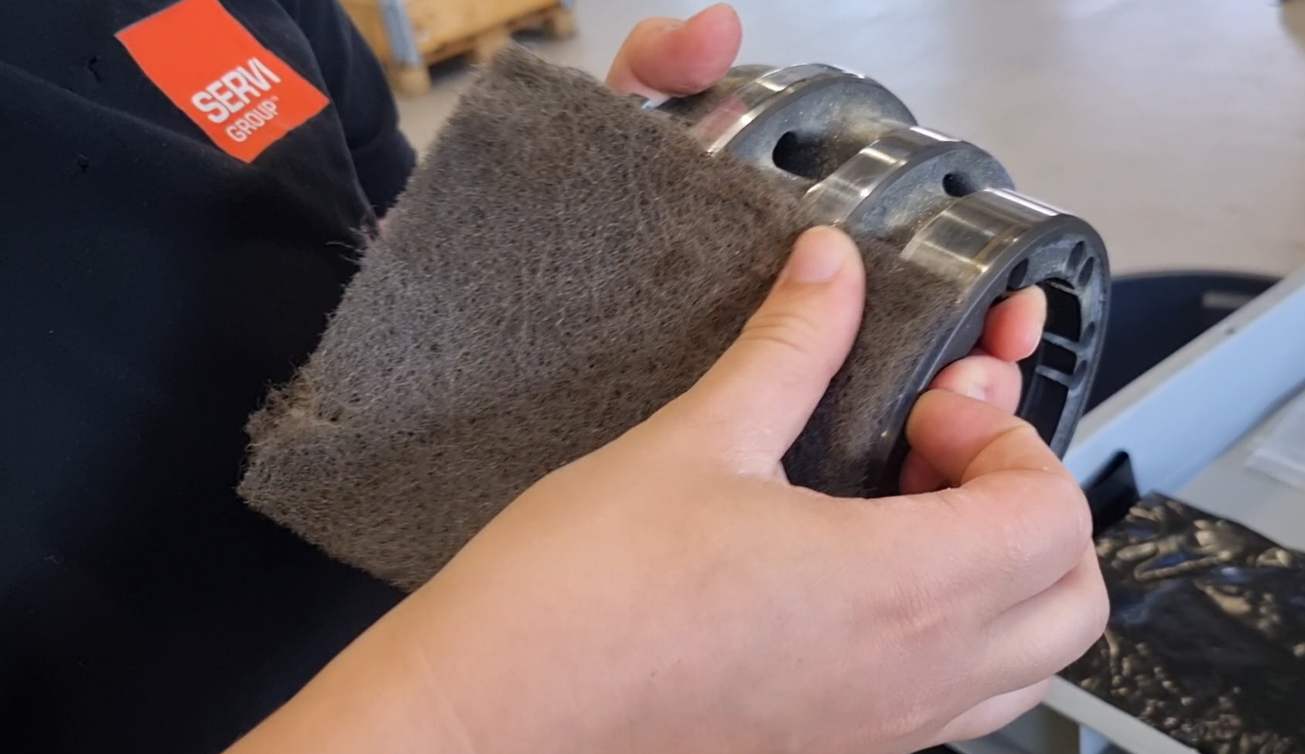 Close-up of scratch being sanded away on Poclain engine with Servi Group logo on t-shirt